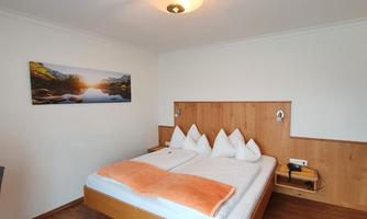 A cozy hotel room with a large double bed and wooden decor. On the wall hangs a picture of a landscape with a river and mountains.