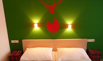 A modern bedroom with a green wall design and a stylized deer head above the bed. The beds are adorned with white pillows, and there are decorative nightstands.