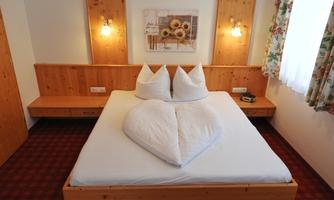 A cozy bedroom with a large bed and handcrafted wooden details. On the bed rests artfully folded heart-shaped pillows.