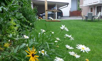A well-maintained garden with colorful flowers and green lawn. In the background, a car and garden furniture are visible.