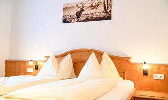 A cozy bedroom with a double bed and two high beds. On the wall hangs a picture of a deer in the wild.