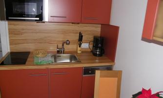 A modern kitchen with red cabinets and a wooden countertop. It is equipped with a stove, a sink, and a coffee machine.