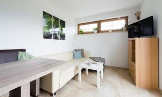 A modern living room with a bright sofa and a table. Pictures hang on the wall and a television stands on a wooden cabinet.