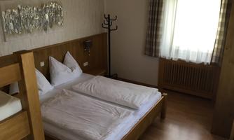 A simple hotel room with two single beds and a bunk bed. There is a clothes rack and a window with curtains.