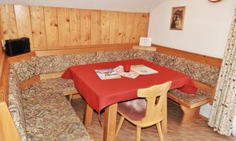 A cozy dining area with a red tablecloth and wooden furniture. The walls are made of wooden panels, and there are cushioned benches around the table.