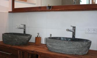A modern bathroom with two round sinks made of gray stone. The wooden base and the large mirror create a warm atmosphere in the space.