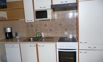 A modern kitchen with white cabinets and a stove. The equipment includes a refrigerator, a microwave, and a sink.
