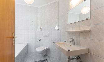 A modern bathroom with bright tiles and a bathtub. There is a sink, a mirror, and a toilet.