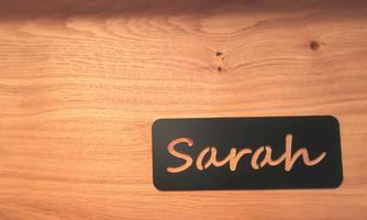 A black-lettered sign with the name "Sarah" on a wooden surface. The wood grain is clearly visible and adds warmth to the background.