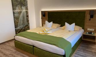 A modern bedroom with two beds and green bedding. In the background, there is a decorative picture of a waterfall.