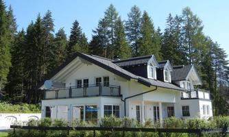 A modern house with a beautiful garden, surrounded by tall trees. The building has a simple, elegant design and large windows.