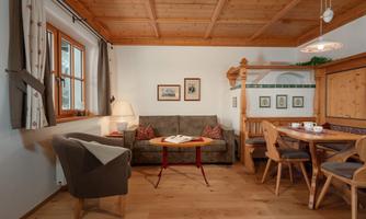 A cozy living space with wooden ceilings and a large sofa. A dining area with chairs and a table complements the inviting atmosphere.