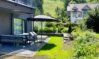 A cozy terrace with a sunshade and garden furniture. The well-maintained garden features a green lawn area and plants.