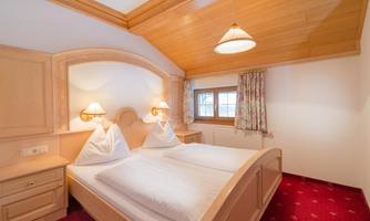 A cozy bedroom with two single beds and a wood-paneled ceiling. Large windows let in plenty of light, and the room's decor is friendly and inviting.
