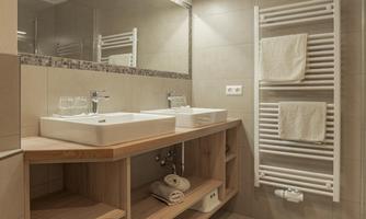 A modern bathroom with two sinks and a large mirror surface. In the background, there is a towel warmer and a bright, inviting design.