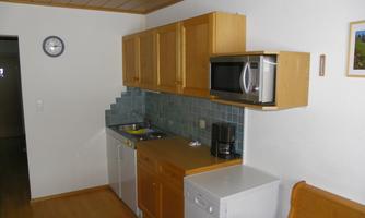 A modern kitchen with wooden cabinets and a microwave. The walls are light and the fittings are functional.
