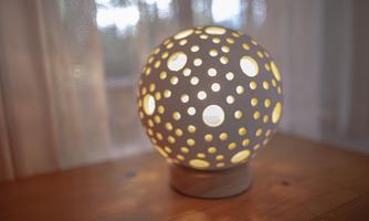A decorative lamp in spherical shape with many holes. It emits warm light and stands on a wooden table.