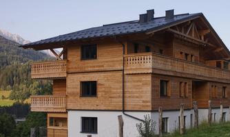 A modern wooden house with several balconies and a beautiful view of the mountains. The facade is a mix of wood and plaster.