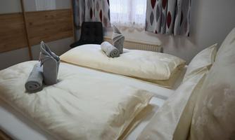 A cozy bedroom with two beds and soft pillows. The bedding is light and the windows let in plenty of natural light.