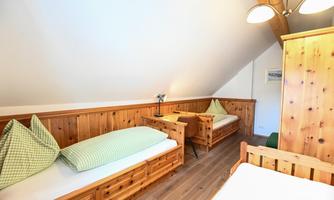 A cozy room in the attic with wooden paneling. It is equipped with two single beds, a table, and a wardrobe.