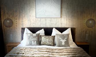 A cozy bedroom with a large bed and decorative pillows. The walls are made of wood, and a piece of art hangs above the bed.