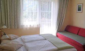 A cozy bedroom with a double bed and a red sofa. Large windows let in plenty of daylight and the walls are painted in soft colors.