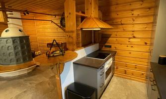 A modern kitchen with wooden paneling and a large table. The equipment includes a stove, a sink, and a waste container.