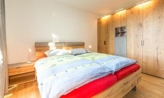 A bright bedroom with a large bed and a wooden furniture wall. The bedding is colorful, and there is gentle lighting.