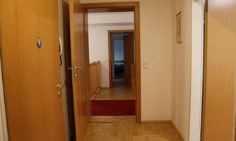 A bright hallway with wooden floors and open doors. In the background, there is a staircase and additional rooms.