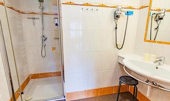 A modern bathroom with a shower, a sink, and a small chair. The walls are brightly tiled, with orange accents.