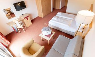 A modern hotel room with a double bed, a sofa, and a table. The room is bright and cheerfully designed.