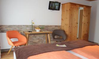 A cozy room with two beds, a wooden table, and two chairs. The walls are bright and modernly designed, and a TV is mounted on the wall.