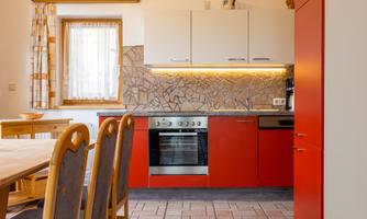 A modern kitchen with a red cabinet and gray countertop. The decor is bright and inviting, with a dining table and chairs in the foreground.