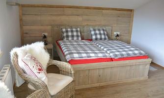 A cozy bedroom with a large double bed and checkered bedding. A comfortable rattan armchair complements the modern rustic design.