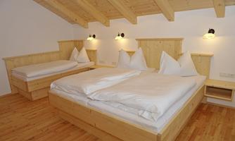 A cozy bedroom with wooden beds and white bedspreads. The walls are painted light, and there is a wooden ceiling with visible beams.