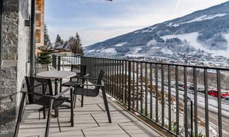 A balcony with modern furniture and a beautiful view of a snowy mountain landscape. The surroundings are calm and inviting.