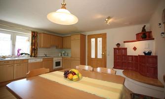 A bright kitchen with wooden cabinets and a large table. On the table, there is a bowl of fresh fruit.