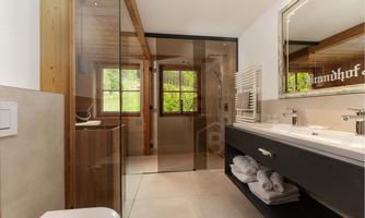A modern bathroom with a glass shower cabin and wooden details. There is an elegant sink with fresh towels and windows that let in natural light.