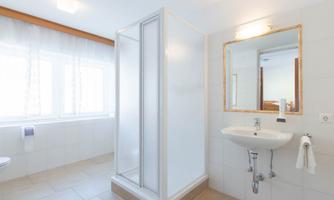 A bright bathroom with a shower cubicle and a sink. Windows provide natural lighting.
