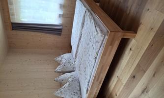 A cozy bedroom with a double bed and two pillows. The room has wood paneling and large windows with curtains.