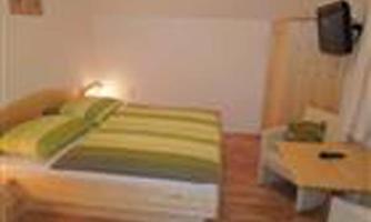 A simple room with a double bed and striped bedcovers. There is a television and a small table in the corner.