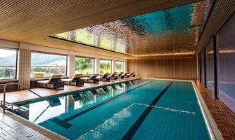 An elegant indoor pool with large windows and a view of nature. Stylish loungers invite relaxation.
