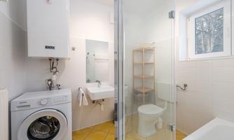 A modern bathroom with a shower, washing machine, and a toilet. The walls are light-tiled, and the floor is made of yellow tiles.