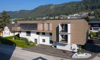 A modern building with a striking facade in a quiet setting. In the background, hills and a green landscape can be seen.
