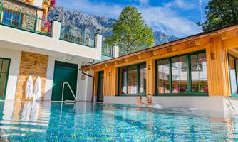 A relaxing outdoor pool with crystal clear water. In the background, mountains and modern wooden architecture can be seen.
