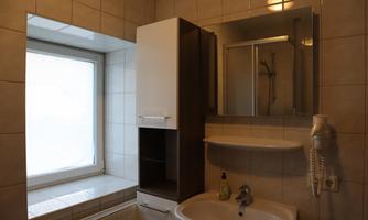 A modern bathroom with bright tiles. There is a sink, a mirror, and a window that lets in natural light.