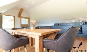 A modern living area with a large wooden table and elegant chairs. In the background, an open kitchen is visible.