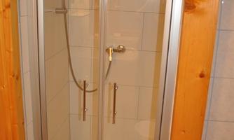 A modern shower with glass partitions and a wooden frame. The space is bright and clean, ideal for a bathroom.