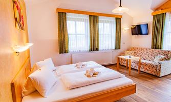 A bright room with two beds, a cozy sofa, and a table. Large windows provide plenty of natural light.