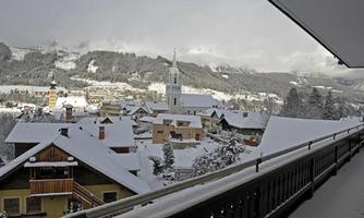 A snowy landscape with a quiet village. In the background, mountains and a church tower rise into the sky.